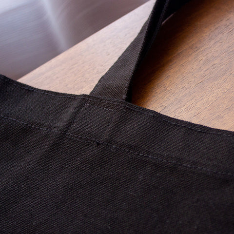 Detalle de la costura del asa de la totebag negra de 38 cm hecha de loneta 100% algodón.